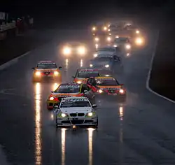 File de voitures zigzaguant sur une piste très mouillé et sous une pluie battante.