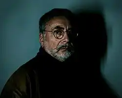 Photographie d'un homme barbu et portant des lunettes, vu de profil, le regard tourné vers l'objectif.