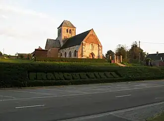 Léger surplomb de l'église.On remarque ses 2 niveaux successifs par rapport à la route. D'abord celui du cimetière, encore entouré de sa haie, auquel on accède par quelques marches.