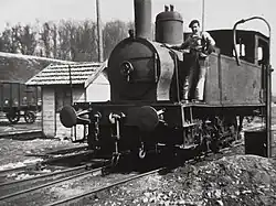 Photo noir et blanc d'une petite locomotive à vapeur vue de face et son chauffeur.