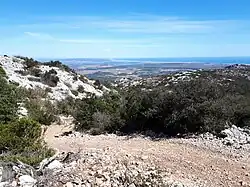 Paysage de garrigue dans l'angle sud-ouest de la commune. Vue vers le nord-est depuis les collines calcaires du Jurassique supérieur et du Crétacé inférieur. Au loin, au centre : le village de Roquefort-des-Corbières (avec Sigean et l'Étang de Bages-Sigean au-delà).