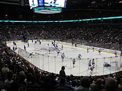 vue en plongée sur un stade de hockey durant une compétition. Les joueurs d'une équipe sont habillés en rouge et blanc, les autres en bleu