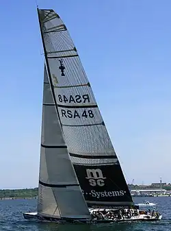 Bateau progressant sous voile non loin du rivage.