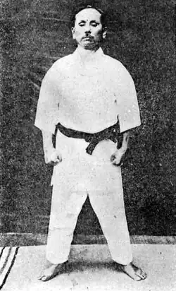 Gichin Funakoshi dans la position du yoi, qu'on retrouve au début de chaque kata Heian. Debout, pieds écartés de la largeur du bassin, bras le long du corps et poing serrés.