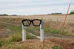 Une sculpture représentant deux poteaux blancs tenant une monture de lunettes noires comme celles de Buddy Holly.