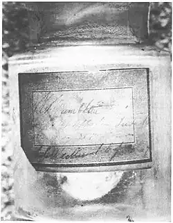 Photographie en noir et blanc d'un flacon portant une étiquette.