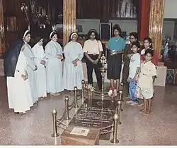 Photo en couleurs d'un groupe de religieuses et de jeunes autour d'une dalle funéraire