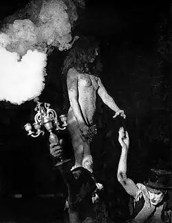 Des acteurs déchaînés, l'un d'eux tient un fumigène et porte une femme nue debout sur ses épaules.