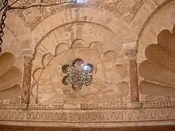 Photographie d'un oculus hexalobé à claustra, rempli de verres de couleur. Il orne l'espace compris entre les trompes cannelées, en coquille, de la coupole du mihrab.