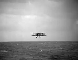 Photo en noir et blanc d'un avion biplan volant au-dessus de l'océan.