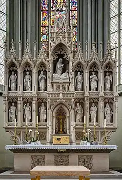 Au dessus d'une table une scuplture en forme de panneau compartimenté de différente figurines.