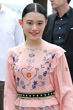 Photographie couleur d'un portrait de taille d'une jeune femme typée asiatique, avec une tunique rose à motifs floraux.