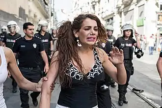 Une femme avec une expression de détresse marche dans la rue, suivie d'une dizaine de policiers