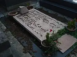Photographie en couleur d'une pierre tombale finement sculptée avec des motifs mayas, et entourée de quelques fleurs rouges.