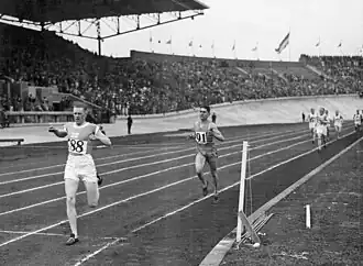 Photographie en noir et blanc de l’arrivée d'une course à pied dans un stade à huis clos.
