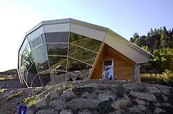 Photographie d’une maison adossée à une montage et dont toute la façade sud est vitrée.