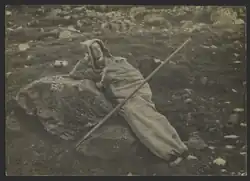 Photographie d'un homme coucher dans l'herbe, appuyé sur un rocher, enfoui dans un sac en peau d'animal.
