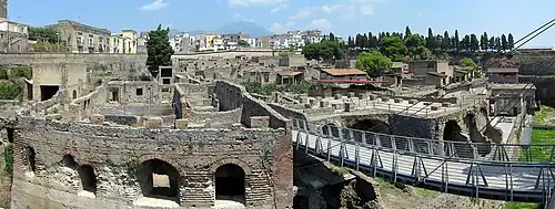 panorama sur hauts de murs en ruine, au fond bâtiments modernes et arbres
