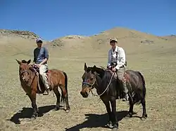 Un couple occidental sur des chevaux mongols, souriant.