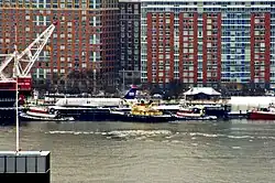 Photo de l'avion après sa récupération du fleuve, au premier plan. Ce dernier est installé au bord du quai et plusieurs navires sont présents sur la rivière.