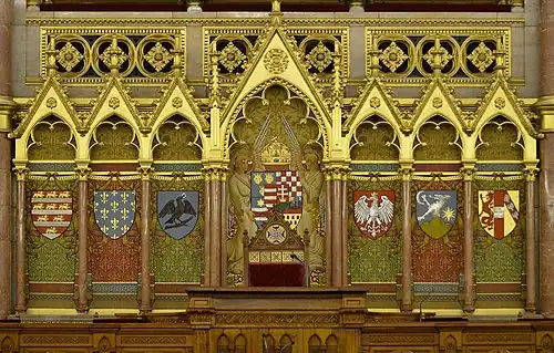 Derrière le pupitre du président de la Chambre des magnats sont représentés les blasons des principales familles ayant régné sur la Hongrie. Encadrant les armes du royaume, de gauche à droite : Arpadiens, Anjou, Hunyadi,  Jagellons, Zapolya, Habsbourg.