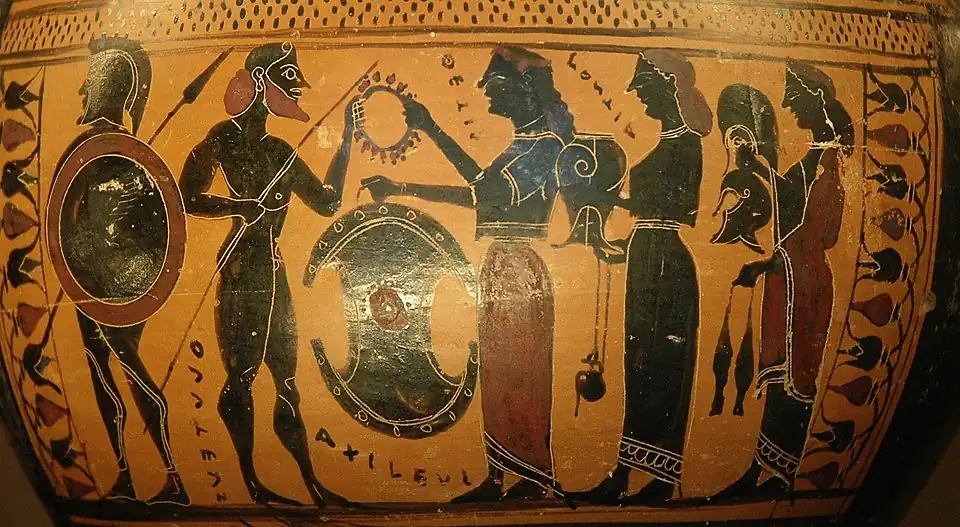 Photographie d'une scène peinte sur un vase grec antique à figures noires montrant plusieurs personnages debout. Au centre, Achille, barbu, tourné vers la droite, tient une lance dans sa main droite. De la main gauche, il prend une couronne que lui donne la déesse Thétis, sa mère, qui lui fait face sur la droite. Thétis, vêtue d'une tunique longue, a les cheveux longs. Elle remet la couronne à Achille de la main droite. Dans sa main gauche, elle tient un grand bouclier rond qu'elle s'apprête à lui remettre. Sur la gauche, derrière Achille, un guerrier en armure complète portant des protège-genoux, un bouclier rond, un casque à panache et une lance se tient tourné vers la gauche, dos à la scène. Derrière Thétis sur la droite, deux servantes aux cheveux longs, vêtues de tuniques, s'avancent en portant d'autres pièces d'équipement destinées à Achille. La première porte la cuirasse, la deuxième tient un bouclier dans la main droite. Chacune tient l'objet dans sa main droite, et, dans la main gauche, porte un récipient suspendu au bout d'une cordelette et destiné sans doute à accomplir un rituel. Le bord de la scène à gauche et à droite est marqué par un motif floral. Sur le dessus, une double ligne horizontale surmontée de rangées de points noirs. Des inscriptions grecques inscrites verticalement entre les personnages nomment Achille, Thétis, le guerrier de gauche et la première servante.