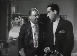Une scène en noir et blanc du film Il padrone del vapore. La scène se trouve à l'intérieur. Deux hommes en costume se regardent sans expression sur leur visage. Une femme, un peu en arrière, les fixe.