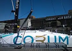 Milieu du bateau, de profil, amarré au ponton. Rouf et protection du cockpit ne sont que légèrement surélevés par rapport au pont.