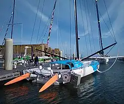 Vu de trois quarts arrière, voilier blanc et bleu amarré au ponton.