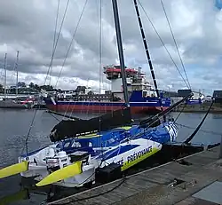 Vu de trois quarts arrière, voilier bleu, blanc et jaune amarré au ponton.