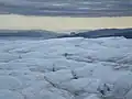 La terre, à l'horizon, est à plusieurs dizaines de kilomètres. Les notions de distances sont bouleversées. La petite colline au centre peu avant l'horizon est le pain de sucre de Kangerlussuaq.