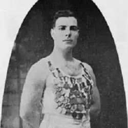 Un homme pose debout avec un maillot présentant de nombreuses médailles.