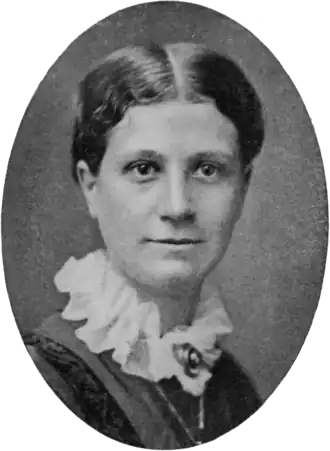 Portrait photographique de face d'une jeune femme blanche portant une collerette blanche ornée d'un bijou