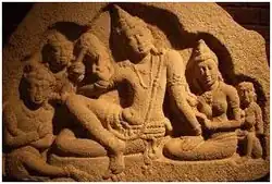 5 personnages assis. Au centre le roi, entouré de son épouse et d'un enfant et de deux serviteurs de l'autre côté.