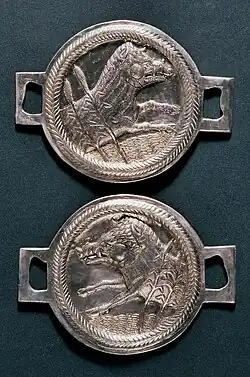 Photographie de deux bijoux en argent de forme circulaire et, dans chacun desquels, est représenté un sanglier gravé de profil.