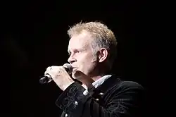 Photo d'un homme parlant dans un micro qu'il tient dans la main gauche.