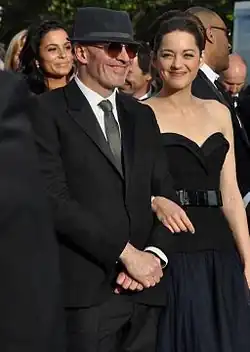  Photographie en couleurs de quatre personnes vêtues élégamment, dont un enfant, sur un grand escalier au tapis rouge.