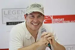 Photo d'un homme en chemisette, souriant, un micro en main