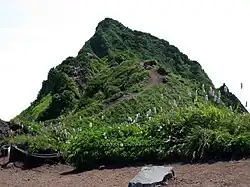 Photo couleur d'un sommet de montagne, un pic rocheux recouvert de verdure.