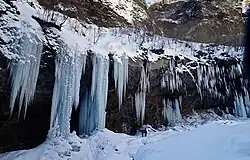 Photo couleur de stalactites de glace le long d'une paroi rocheuse enneigée.
