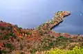 Photo couleur de la rive boisée (couleurs automnales : orange, jaune, brun et vert) d'un lac aux eaux bleues ; au centre, la rive se prolonge par une péninsule toute aussi boisée.
