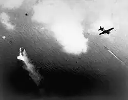 Photographie en noir et blanc prise d'un avion à moyenne altitude. Un autre avion précède celui d'où a été pris la photo et un navire est visible.