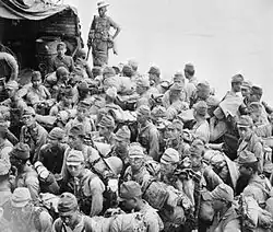 Photographie d’époque de la 53e division. Les soldats sont assis, entassés sur une petite embarcation.