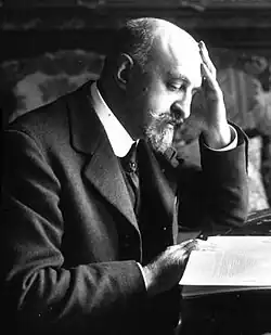 Photo noir et blanc d'un homme en costume, penché sur des feuillets en train de lire.