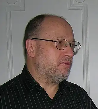 Photographie de profil d'un homme aux cheveux dégarnis, à la barbe courte et portant des lunettes.