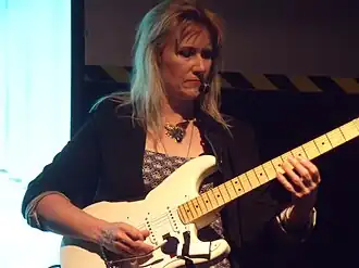 Photo d'une femme blanche adulte jouant de la guitare électrique (Stratocaster blanc crème avec manche en érable)