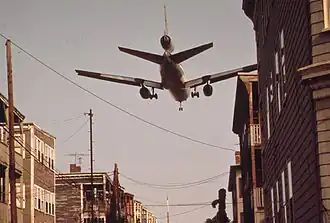 Un McDonnell Douglas DC-10 atterrissant sur l'aéroport Logan, au-dessus de la rue Neptune, à EastBoston. Les maisons bordant la voie seront rachetées par le Massachusetts Port Authority, et toutes démolies. Photo mai 1973.
