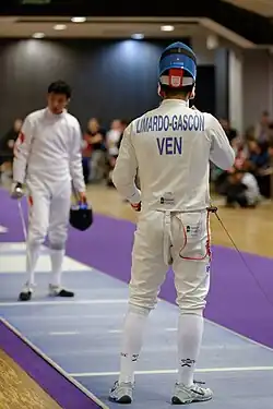 2 escrimeurs, l'un de face, l'autre de dos au premier plan, avant un assaut.