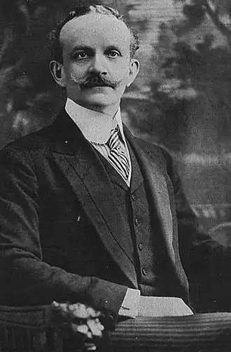 photographie en noir et blanc d'un homme assis sur un siège, vêtu d'un costume.