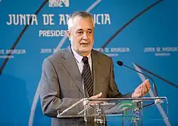 Homme âgé prononçant un discours debout derrière un pupitre.